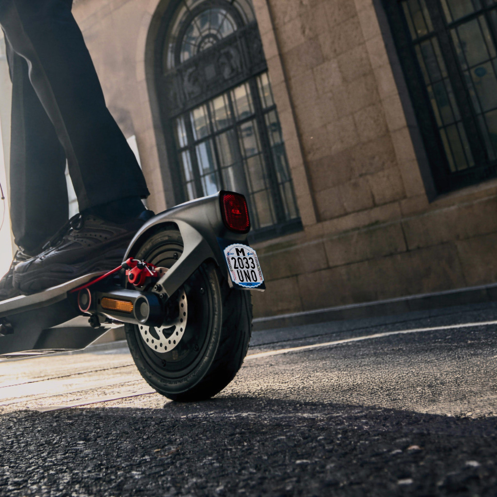 Etiqueta identificativa VMP DGT en patinete eléctrico circulando por ciudad — matrícula patinete obligatoria 2026